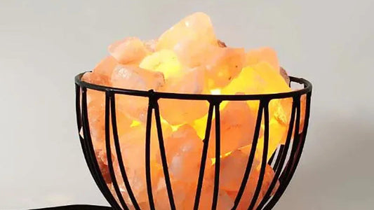 A wire bowl salt lamp filled with glowing Himalayan salt chunks against a pale wall