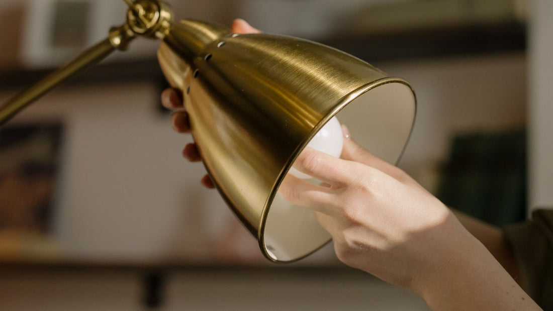 A hand fitting a small bulb into the socket of a metal desk lamp shade