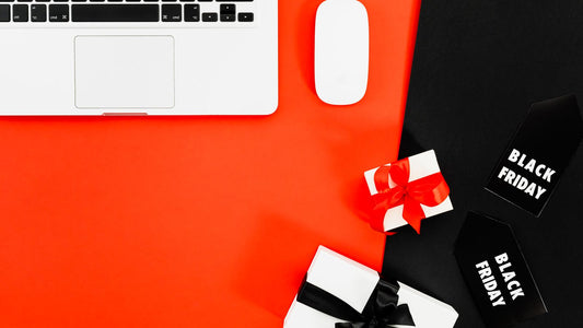 A laptop on a red and black desk beside two wrapped gift boxes and two black Black Friday tags