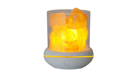 A salt lamp lit from inside, rough chunks of rock salt glowing amber in a clear cylinder on a gray base