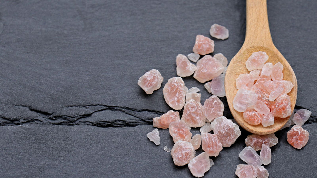 Rough pink Himalayan salt chunks on a wooden spoon and dark slate, showing color variation