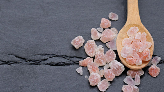 Rough pink Himalayan salt chunks on a wooden spoon and dark slate, showing color variation