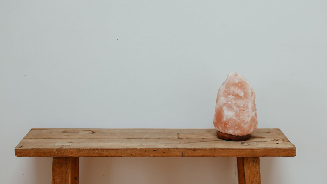 A natural-cut Himalayan salt lamp standing on a rustic wooden bench against a plain wall