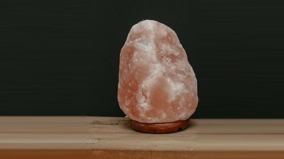 A large natural-shape pink salt lamp on a round wooden base, unlit, on a wooden bench against a dark wall