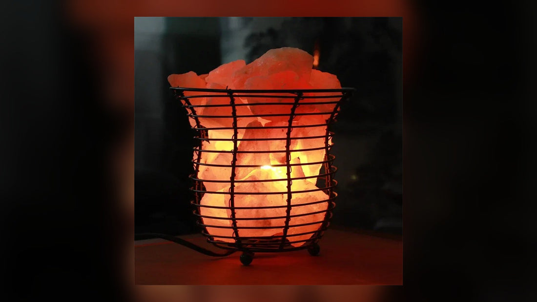 A wire basket Himalayan salt lamp lit on a wooden table in a dim room, its cord trailing across the surface
