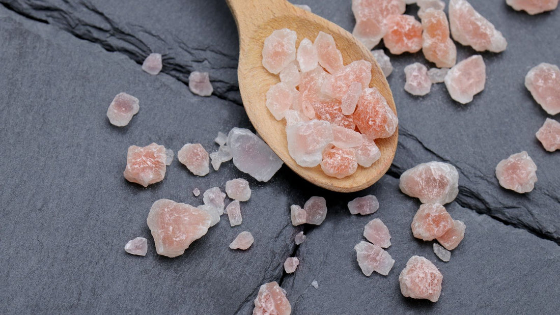Pink Himalayan salt crystals on a wooden spoon scattered across dark slate