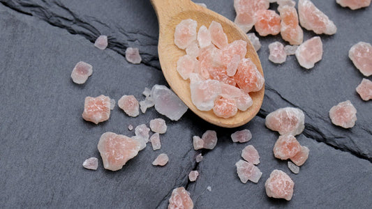 Pink Himalayan salt crystals on a wooden spoon scattered across dark slate