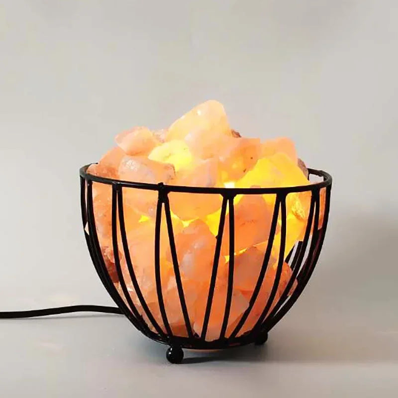 A wire basket salt lamp filled with glowing Himalayan salt chunks, cord trailing to one side