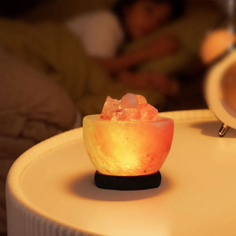 A bowl-style Himalayan salt lamp glowing on a white bedside table, standing directly on the surface