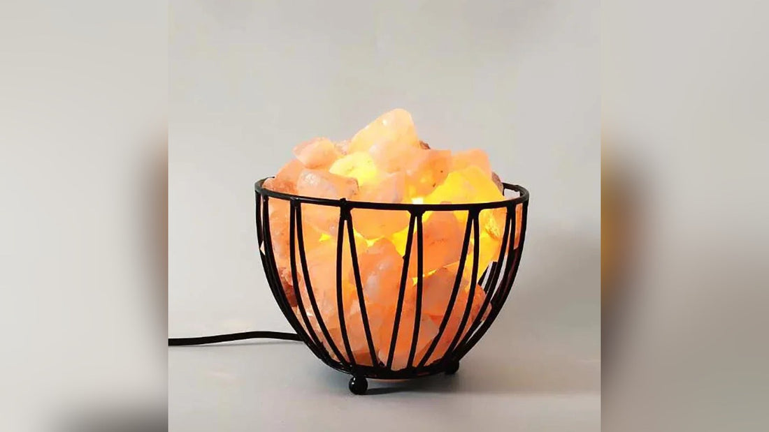 A lit wire bowl salt lamp holding glowing pink salt chunks, its cord trailing across a grey surface
