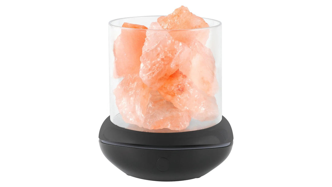 Unlit Himalayan salt lamp with rough pink salt chunks in a clear cylinder on a dark base