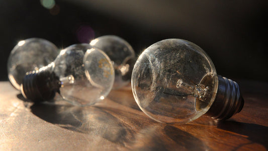 Four spent incandescent bulbs lying on a wooden table in low evening light